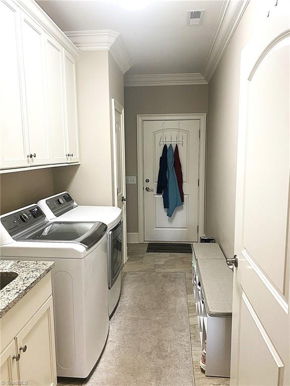 clothes washing area with ornamental molding, cabinet space, visible vents, and washing machine and clothes dryer