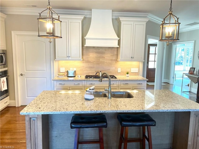 kitchen with dark wood-style floors, an island with sink, custom range hood, crown molding, and backsplash