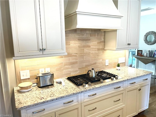 kitchen featuring premium range hood, light stone counters, backsplash, and stainless steel gas stovetop