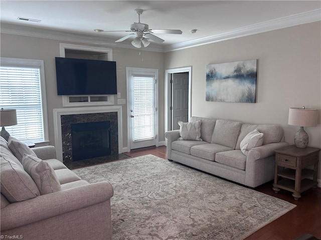 living room with wood finished floors, visible vents, a high end fireplace, ceiling fan, and crown molding