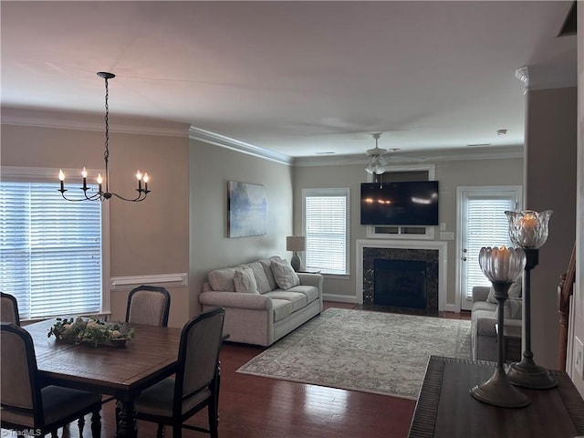 dining area featuring a premium fireplace, ornamental molding, ceiling fan with notable chandelier, and wood finished floors