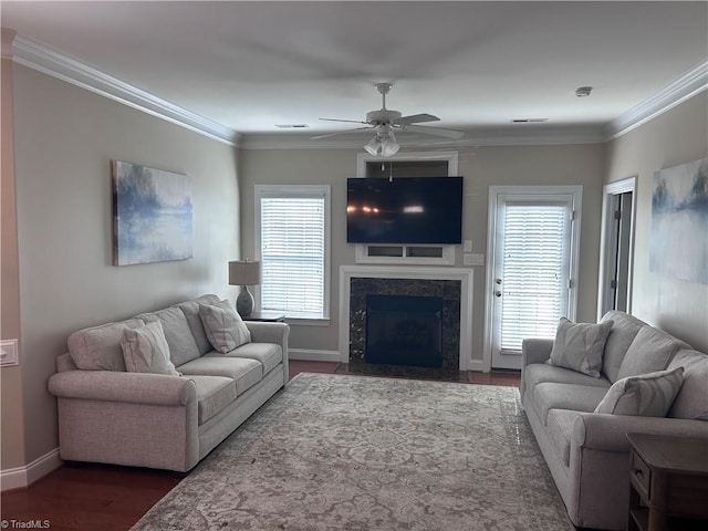 living area with ornamental molding, wood finished floors, a high end fireplace, baseboards, and ceiling fan