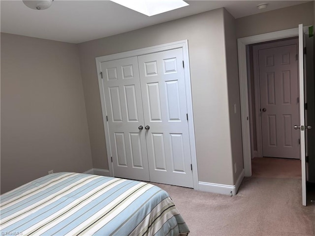 bedroom featuring a skylight, baseboards, a closet, and light carpet