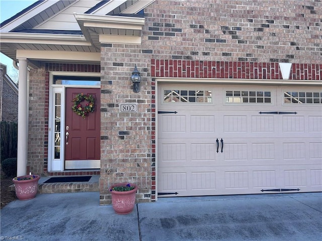 view of exterior entry with concrete driveway, an attached garage, and brick siding