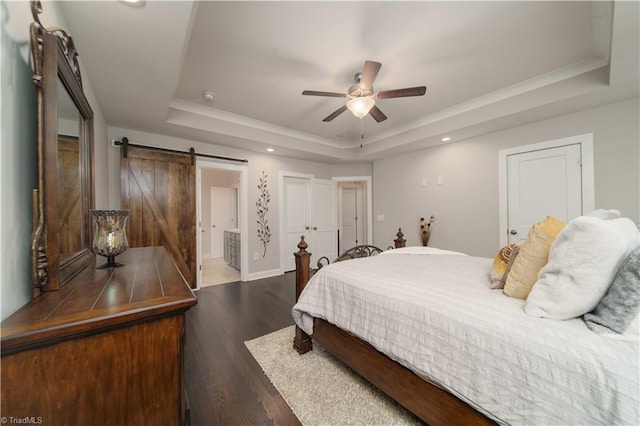 bedroom featuring dark wood-type flooring, ceiling fan, ensuite bathroom, a raised ceiling, and a barn door