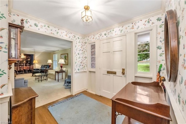 entrance foyer featuring a wainscoted wall, ornamental molding, wood finished floors, and wallpapered walls