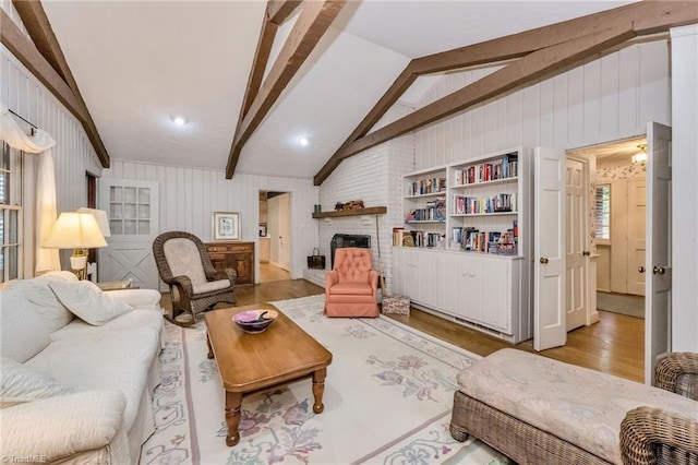 living area featuring lofted ceiling with beams, a brick fireplace, and light wood-style flooring