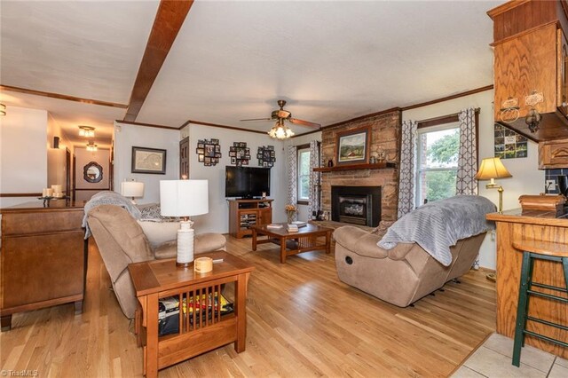 living room featuring ornamental molding, light hardwood / wood-style flooring, ceiling fan, and a stone fireplace