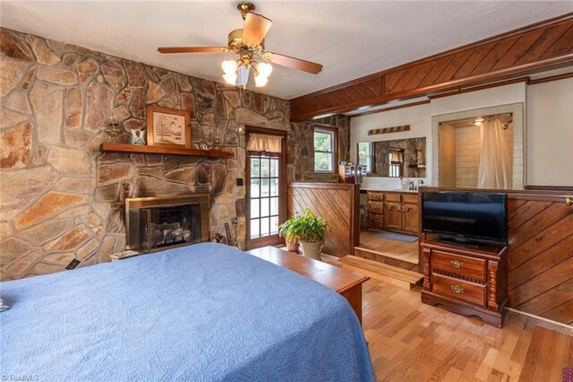 bedroom with light hardwood / wood-style flooring, wooden walls, and a stone fireplace