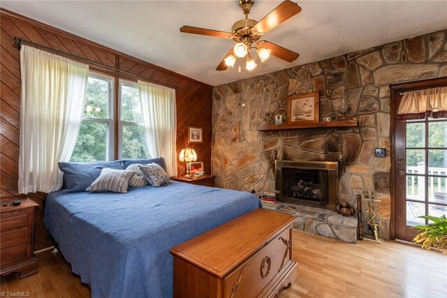 bedroom with light hardwood / wood-style flooring, ceiling fan, wood walls, and a stone fireplace