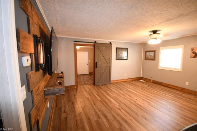 unfurnished living room featuring crown molding, ceiling fan, a textured ceiling, a barn door, and light wood-type flooring