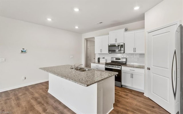 kitchen featuring appliances with stainless steel finishes, sink, light stone counters, and a center island with sink