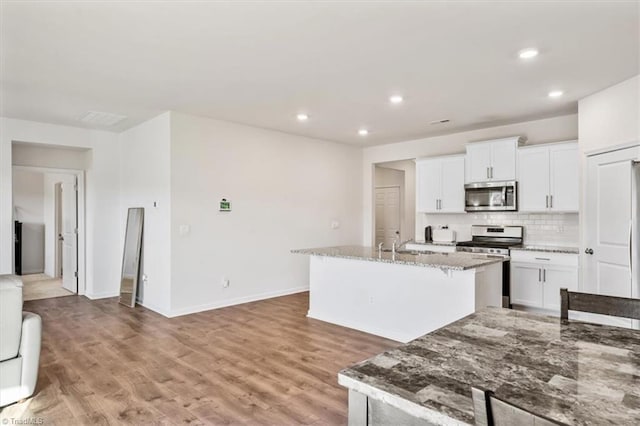 kitchen with appliances with stainless steel finishes, white cabinets, a kitchen island with sink, and light stone counters