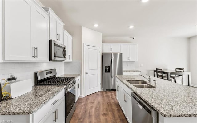 kitchen featuring stainless steel appliances, sink, white cabinetry, light stone counters, and a kitchen island with sink