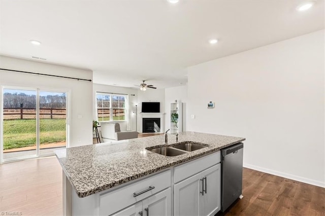 kitchen featuring sink, dishwasher, light stone counters, hardwood / wood-style flooring, and a center island with sink