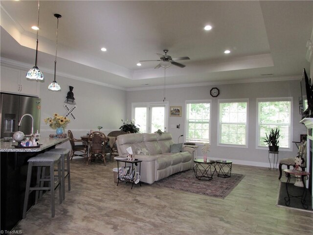 living area featuring a raised ceiling, ceiling fan, recessed lighting, crown molding, and baseboards
