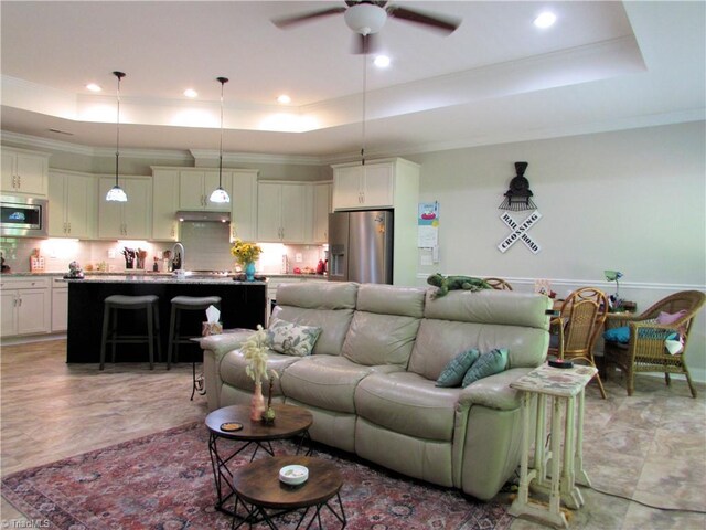 living room featuring a tray ceiling, a ceiling fan, ornamental molding, and recessed lighting