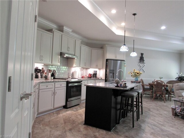 kitchen with stainless steel appliances, under cabinet range hood, crown molding, backsplash, and a kitchen breakfast bar