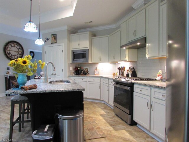 kitchen featuring appliances with stainless steel finishes, a sink, under cabinet range hood, backsplash, and a kitchen bar