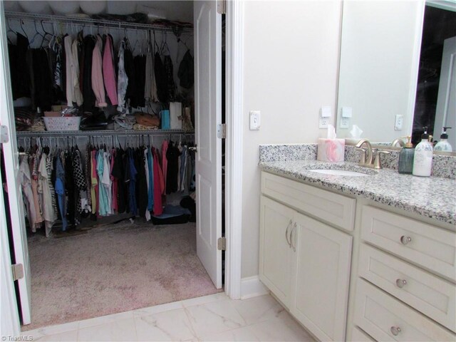 bathroom with a walk in closet, vanity, and marble finish floors