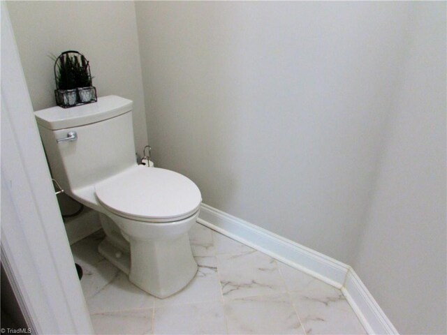 bathroom with marble finish flooring, toilet, and baseboards