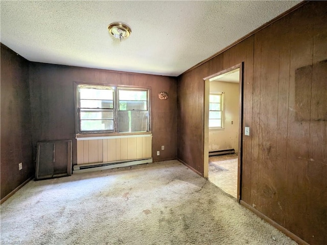 carpeted empty room with wooden walls, a textured ceiling, a baseboard heating unit, and baseboard heating