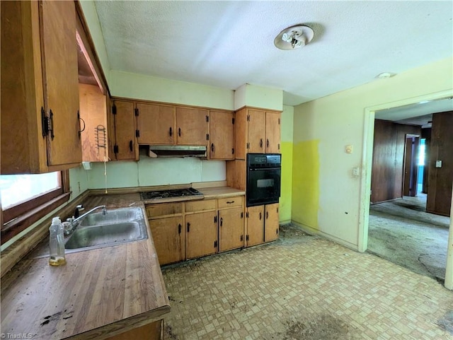 kitchen with oven, gas cooktop, a sink, a textured ceiling, and under cabinet range hood