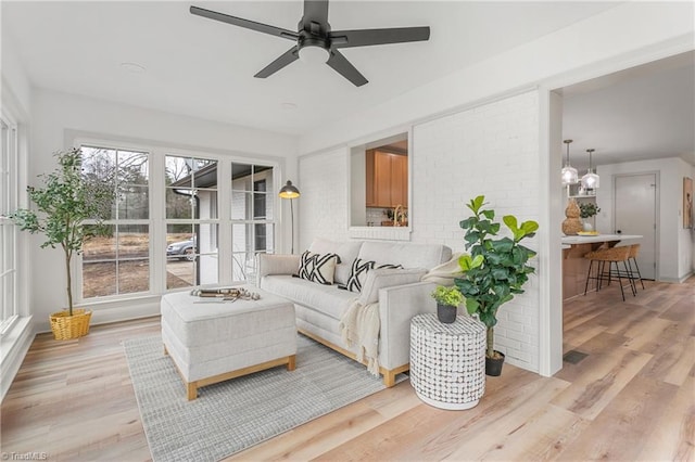 living room with ceiling fan, brick wall, and light hardwood / wood-style floors