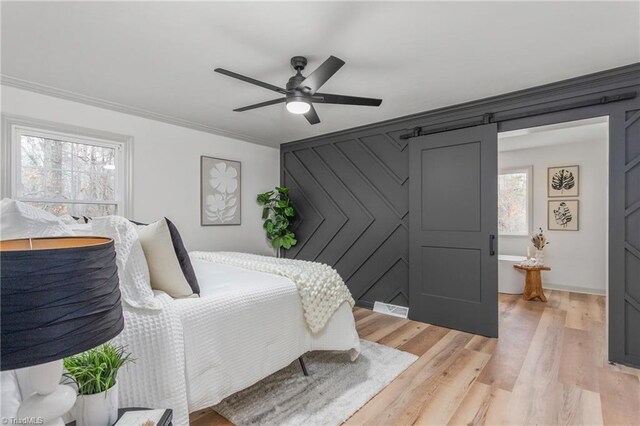 bedroom featuring crown molding, a barn door, ceiling fan, and light wood-type flooring