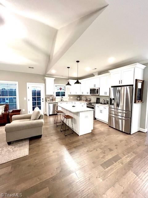 kitchen featuring decorative light fixtures, stainless steel appliances, a breakfast bar, and white cabinets