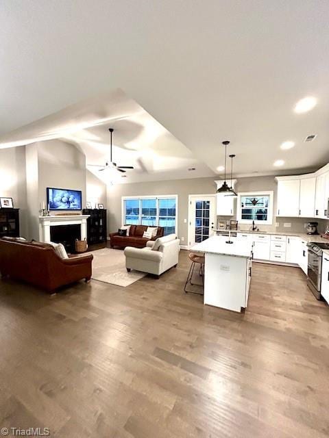 kitchen with a kitchen island with sink, hanging light fixtures, a kitchen bar, white cabinets, and stainless steel range oven