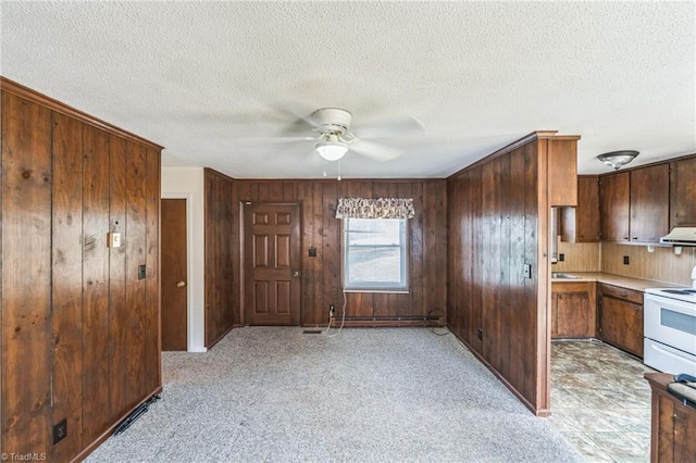 kitchen featuring white electric range, range hood, ceiling fan, a textured ceiling, and wood walls