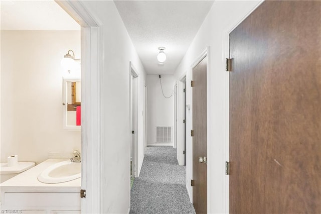 hallway with dark carpet, sink, and a textured ceiling