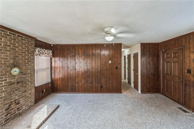 spare room with ceiling fan, a textured ceiling, wooden walls, and light colored carpet