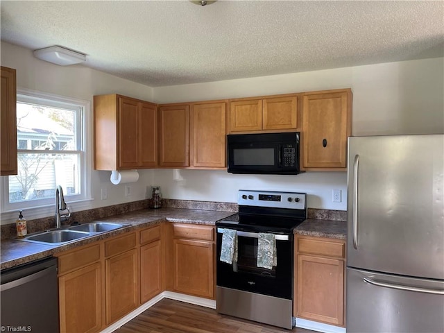 kitchen with sink, appliances with stainless steel finishes, a textured ceiling, and dark hardwood / wood-style flooring