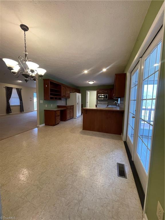 kitchen featuring an inviting chandelier, decorative light fixtures, a textured ceiling, kitchen peninsula, and white refrigerator with ice dispenser