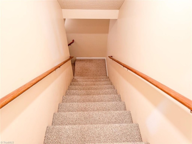 stairway with lofted ceiling, a textured ceiling, and carpet flooring