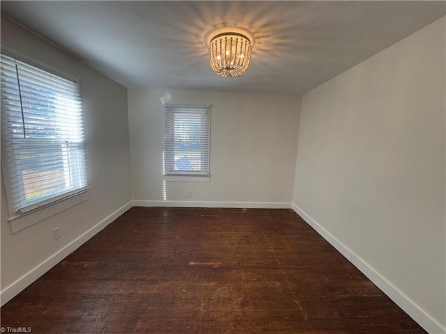 spare room featuring a chandelier and dark wood-type flooring