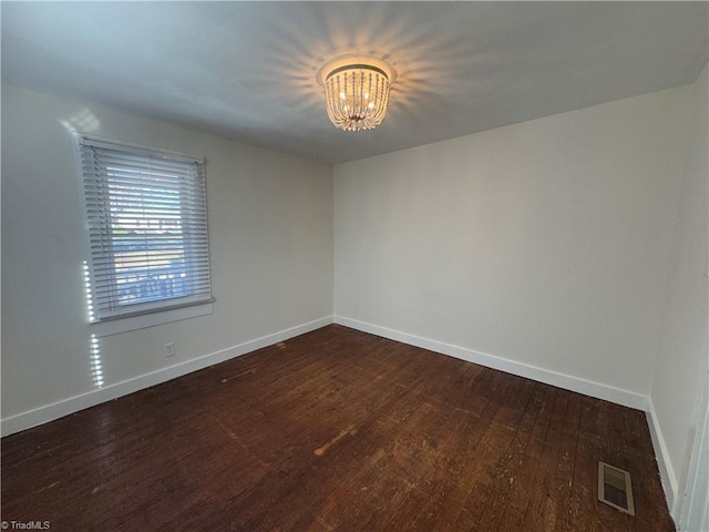 unfurnished room with a notable chandelier and dark wood-type flooring