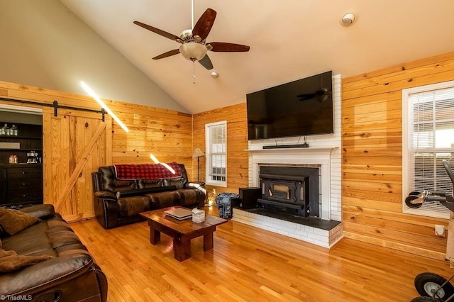 living room with ceiling fan, high vaulted ceiling, a barn door, wood walls, and wood finished floors