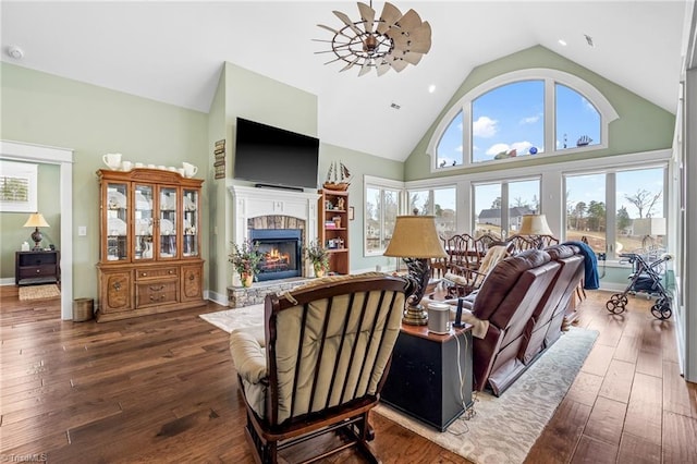 living room featuring ceiling fan, high vaulted ceiling, a stone fireplace, and hardwood / wood-style floors