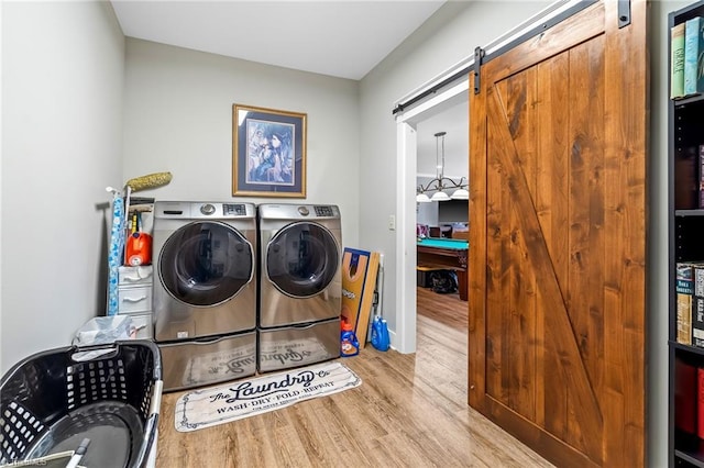 clothes washing area featuring a barn door, washer and dryer, and light hardwood / wood-style flooring