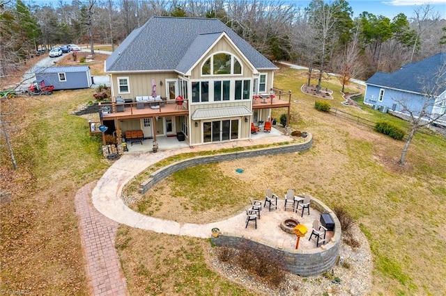 back of property with a lawn, a deck, a shed, a patio, and an outdoor fire pit