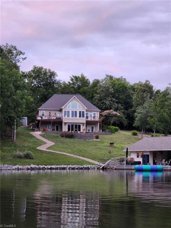 back house at dusk with a water view and a lawn