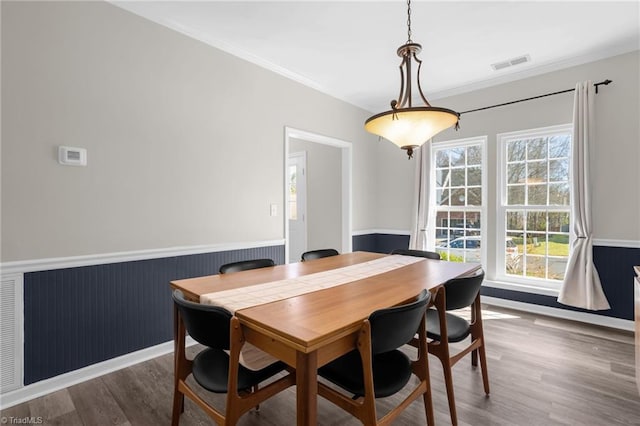 dining room with a wainscoted wall, wood finished floors, visible vents, and ornamental molding