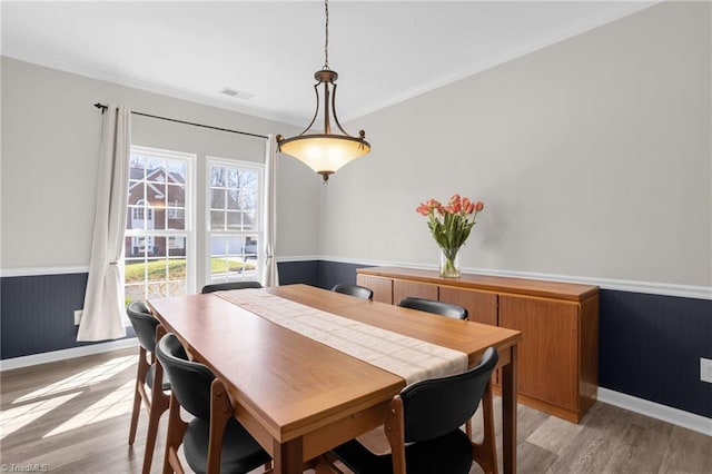 dining area with visible vents, baseboards, ornamental molding, wainscoting, and light wood-style floors