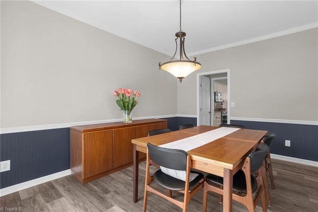 dining area with crown molding, a wainscoted wall, and light wood-type flooring