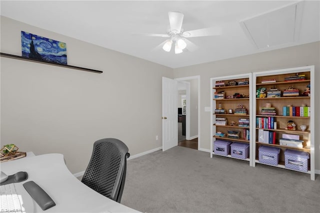 carpeted office space featuring attic access, baseboards, and a ceiling fan