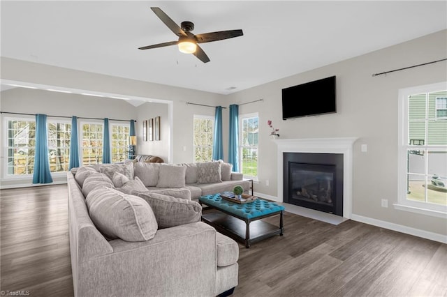living room with baseboards, a ceiling fan, wood finished floors, and a fireplace with flush hearth