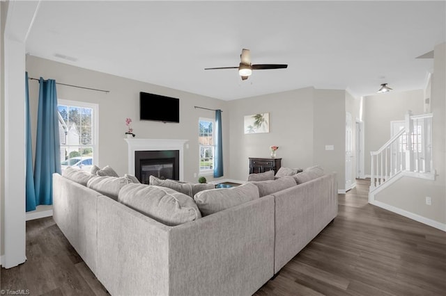 living area with a glass covered fireplace, visible vents, baseboards, and dark wood finished floors